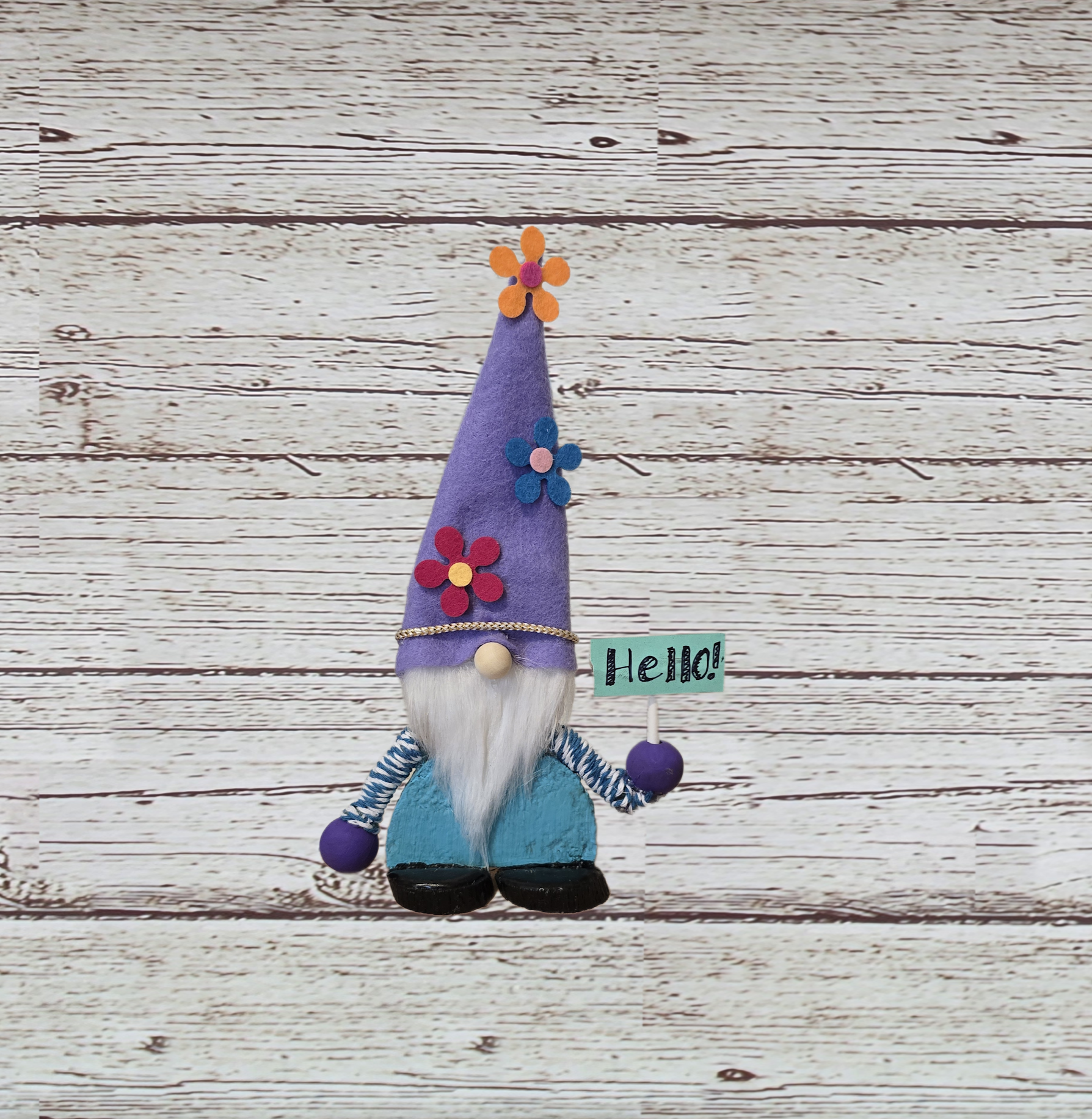 Decorative gnome with a purple hat and 'Hello!' sign on a wooden surface