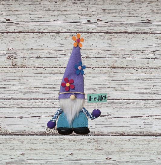 Decorative gnome with a purple hat and 'Hello!' sign on a wooden surface